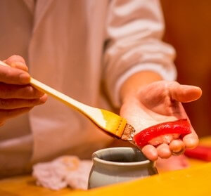 a Sushi chef making Sushi for his customer, dipping soy source on Maguro tuna
