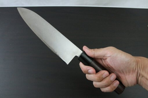 Toshu Santoku multi-purpose Japanese chef's knife, mahogany handle, grabbed by a man's hand