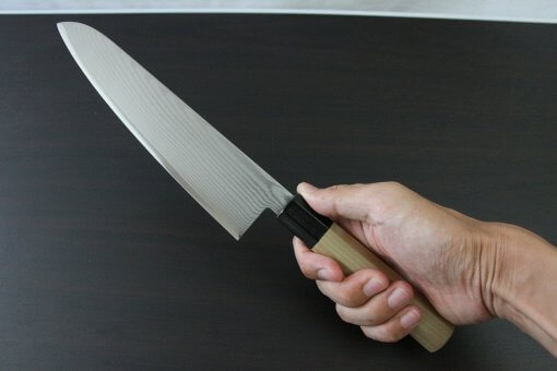 Toshu Santoku multi-purpose Japanese chef's knife, damascus blade and octagonal wood handle, grabbed by a man's hand