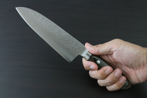 Toshu Santoku multi-purpose Japanese chef's knife, hammered finish blade and gray handle, grabbed by a man's hand