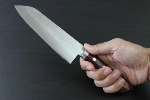 Toshu Santoku multi-purpose Japanese chef's knife, hammered finish blade and mahogany handle, grabbed by a man's hand