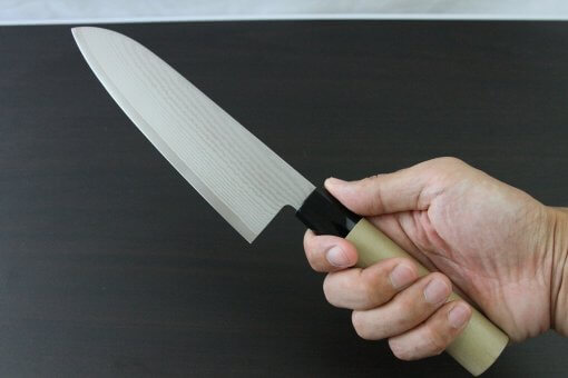 Toshu Santoku multi-purpose Japanese chef's knife, damascus blade and traditional wood handle, grabbed by a man's hand